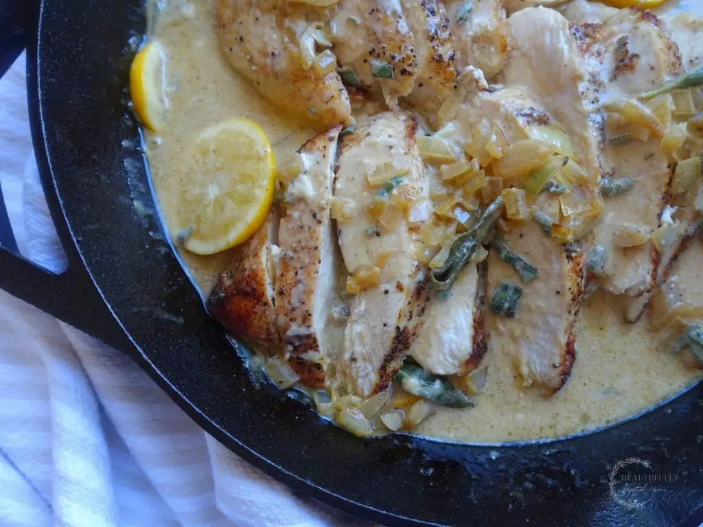 cream sauce flavored with lemons and sage overtop chicken breasts in a cast iron skillet