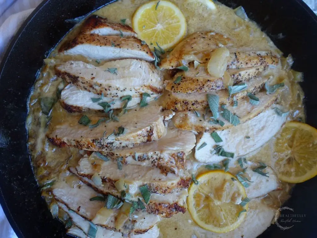 lemon sage cream sauce overtop chicken in a cast iron skillet with lemons and sage