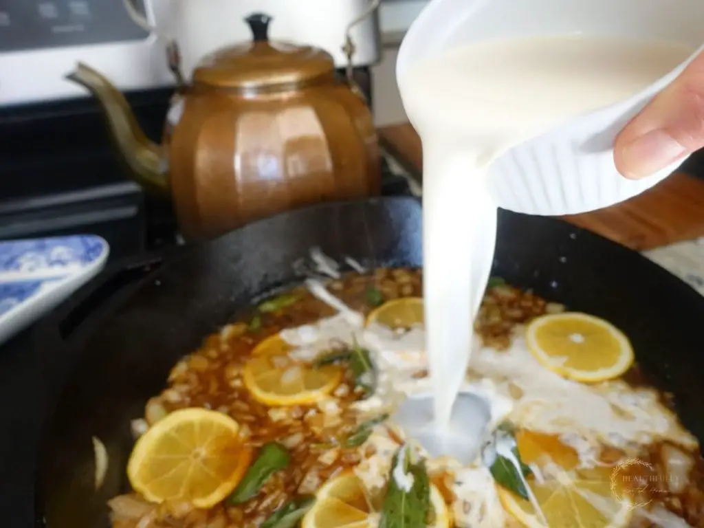 pouring heavy cream into a cast iron skillet with lemon slices and sage