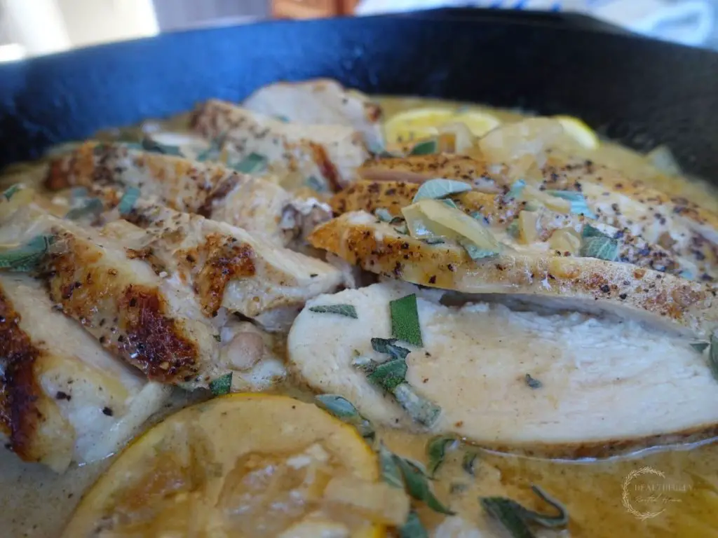 sliced chicken breast inside a cast iron skillet with creamy lemon sage sauce
