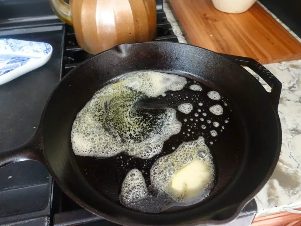 heating sizzling butter in a cast iron skillet with a copper tea kettle in the background