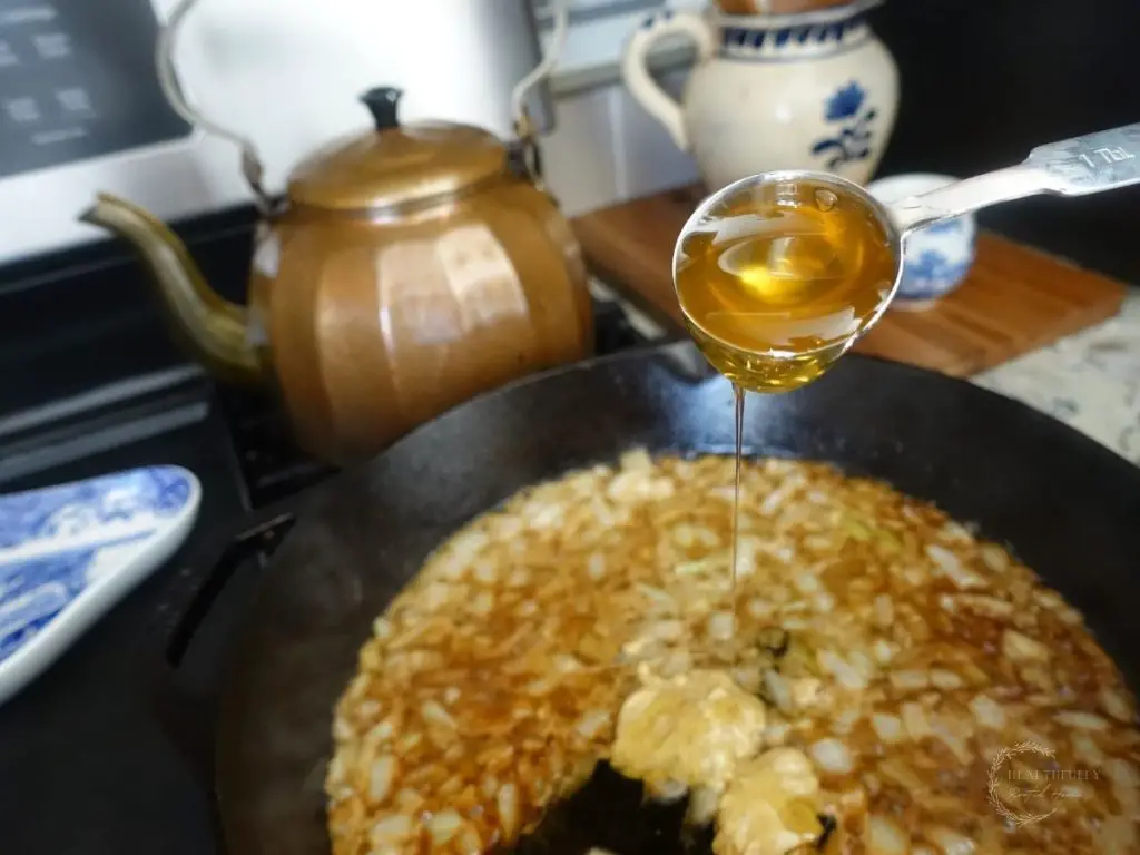 pouring honey into a cast iron skillet with dijon mustard onions and lemon juice
