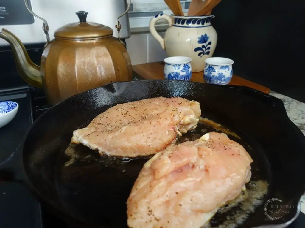 chicken breasts in a cast iron skillet with a copper tea kettle in the background 