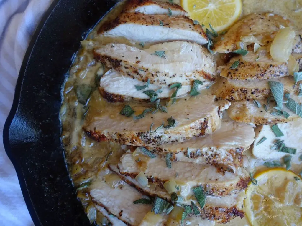 creamy lemon sage sauce chicken in a cast iron skillet with lemon slices and sage as garnish