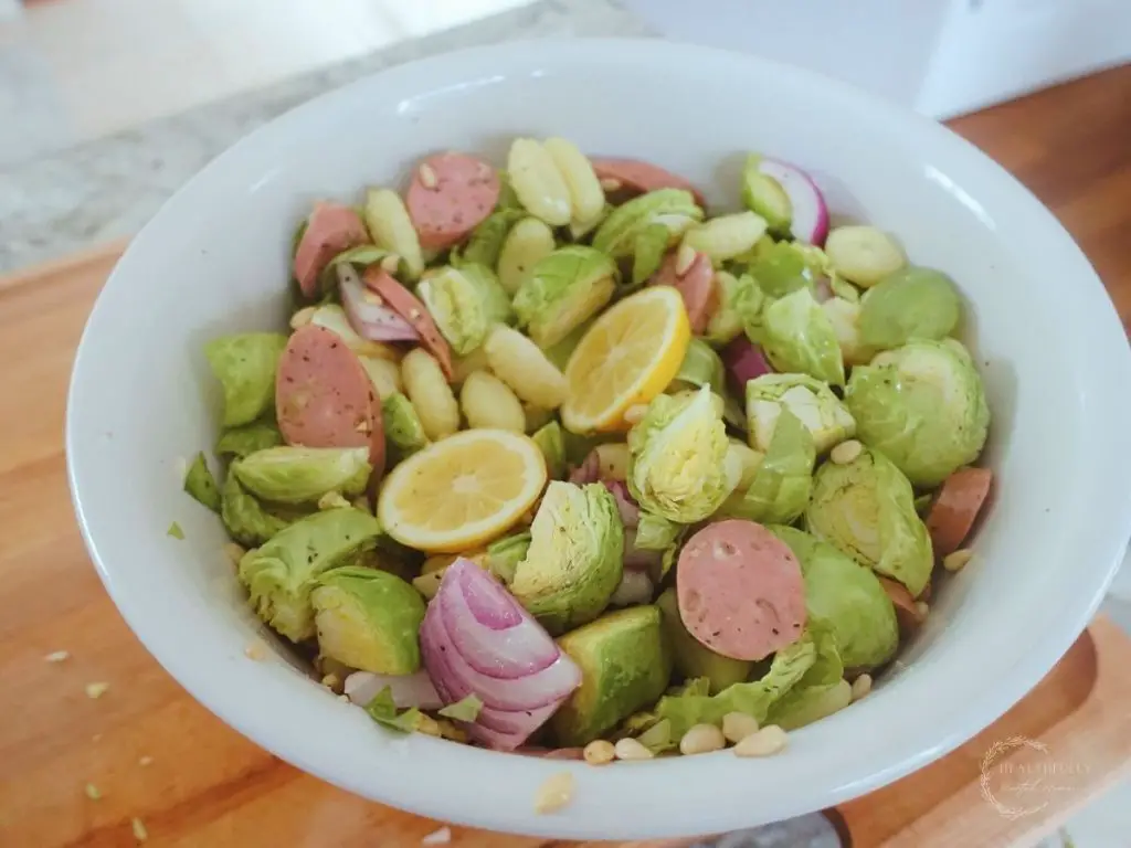 large white bowl with brussels spouts chicken apple sausage lemons and pine nuts