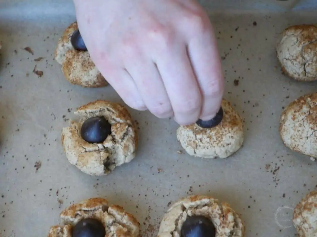 sticking a hershey's kiss in the center of the cooked peanut butter cookies on a parchment lined baking sheet