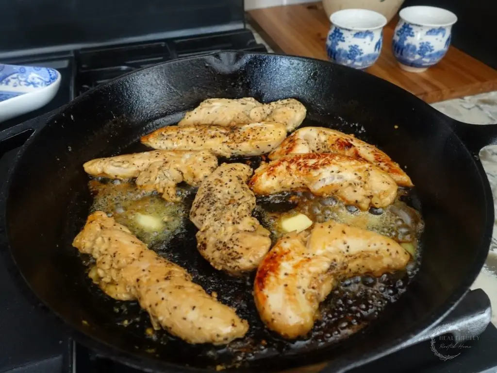 chicken tenders in a cast iron skillet with pads of butter melting on either side