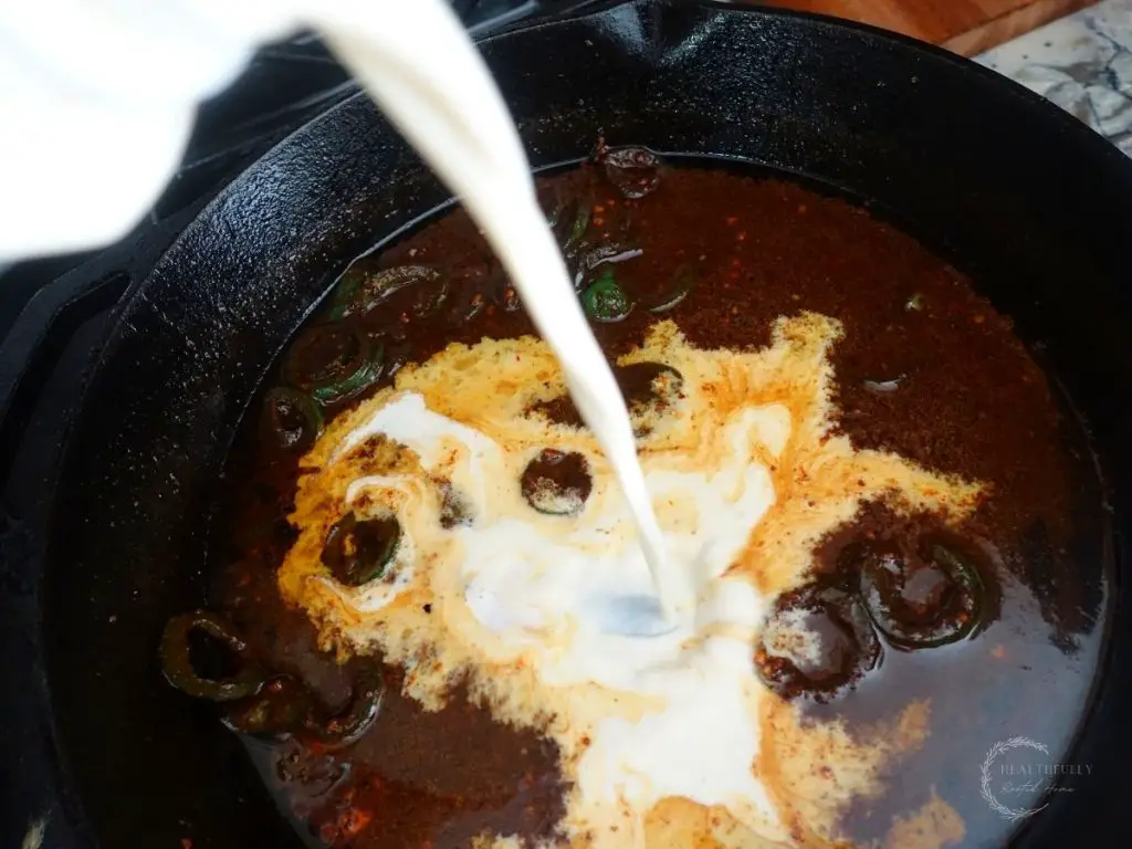 pouring heavy cream into the honey jalapeno sauce mixture inside the cast iron skillet