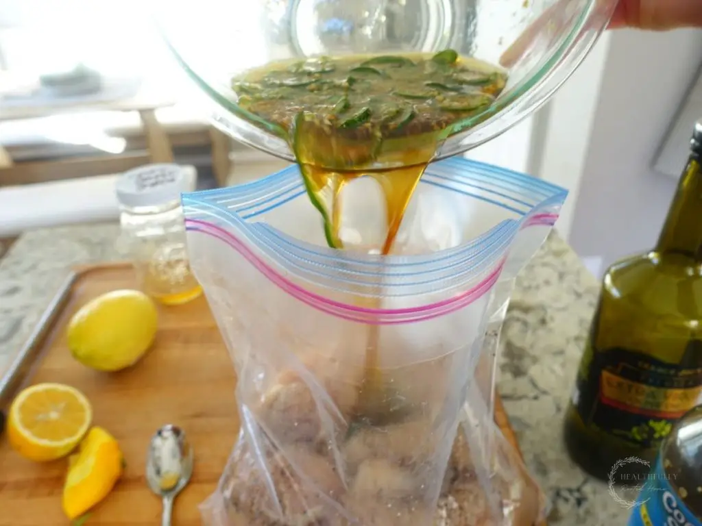 pouring honey jalapeno marinade overtop raw chicken inside a ziplock bag with lemons on the side and a silver spoon next to it