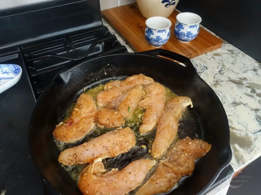 chicken tenders in a cast iron skillet with salt and pepper in the background