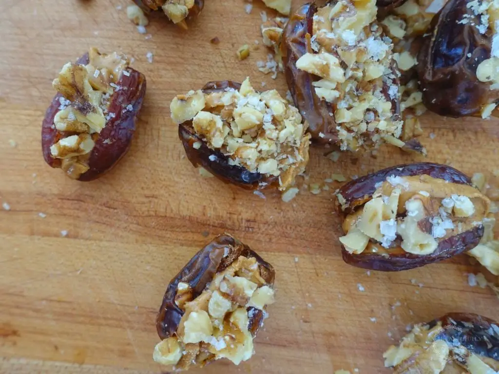 stuffed dates on a wooden cutting board with walnuts peanut butter and sea salt