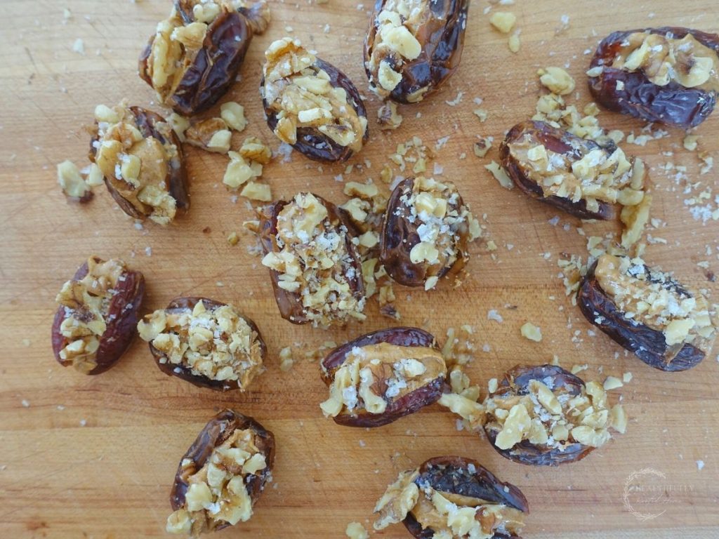 peanut butter stuffed dates topped with walnuts and sea salt on top of a wooden cutting board with chopped walnuts surrounding them