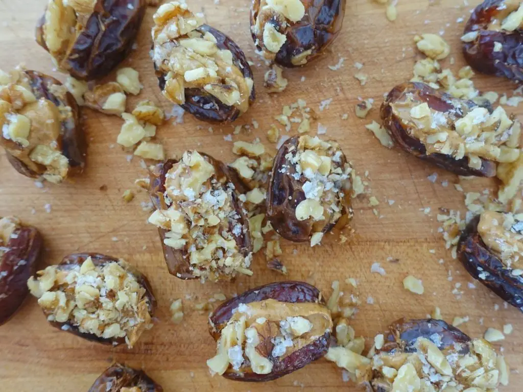 peanut butter stuffed dates with walnuts and sea salt spread out on a wooden cutting board