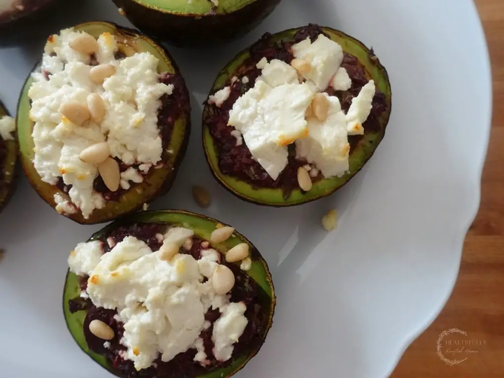 pine nuts on top of stuffed avocados on a white plate