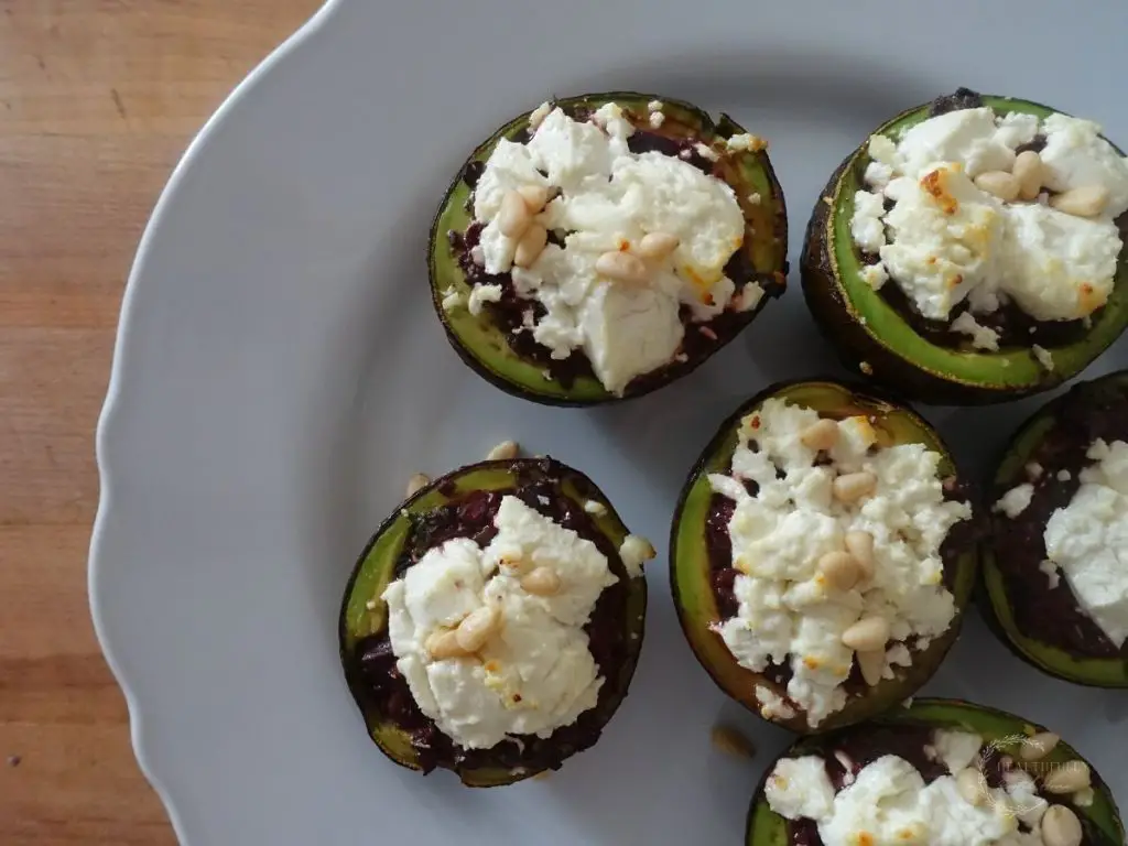 stuffed roasted avocados on a white plate with goat cheese and pine nuts on top 