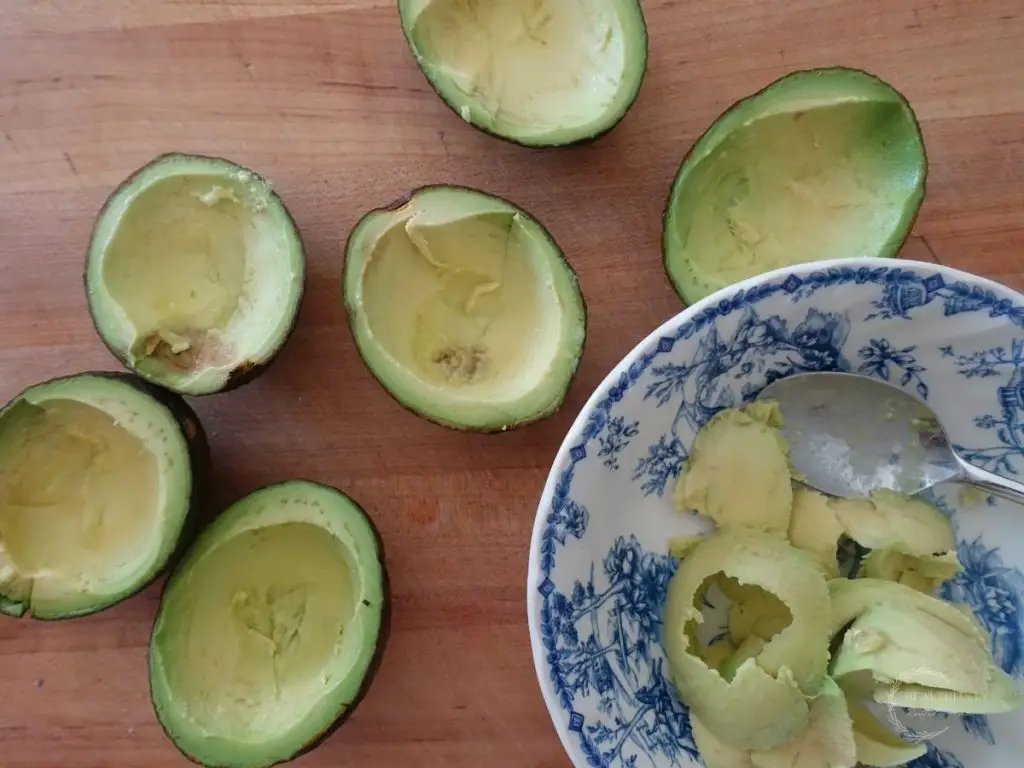 avocados on a wooden cutting board with a bowl of the avocado fruit inside