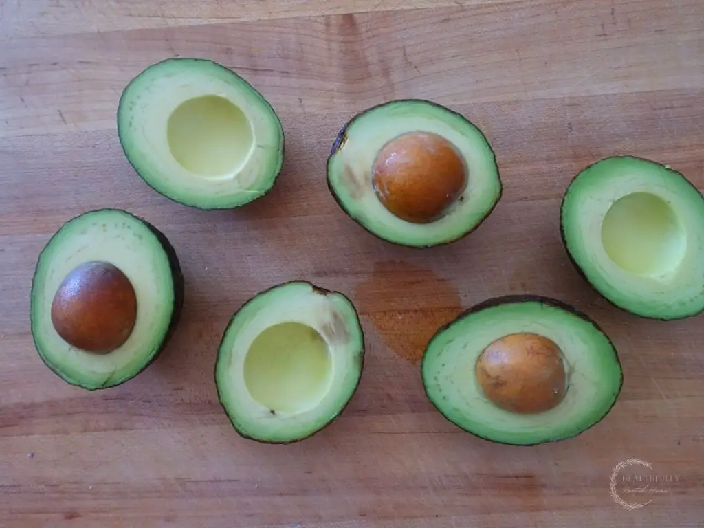 6 halved avocados on a wooden cutting board 
