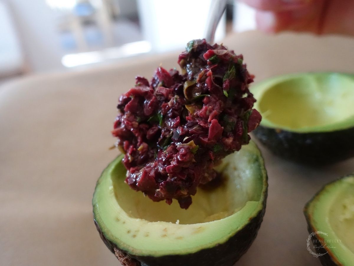 stuffing avocados with kalamata olive tapenade using a silver spoon