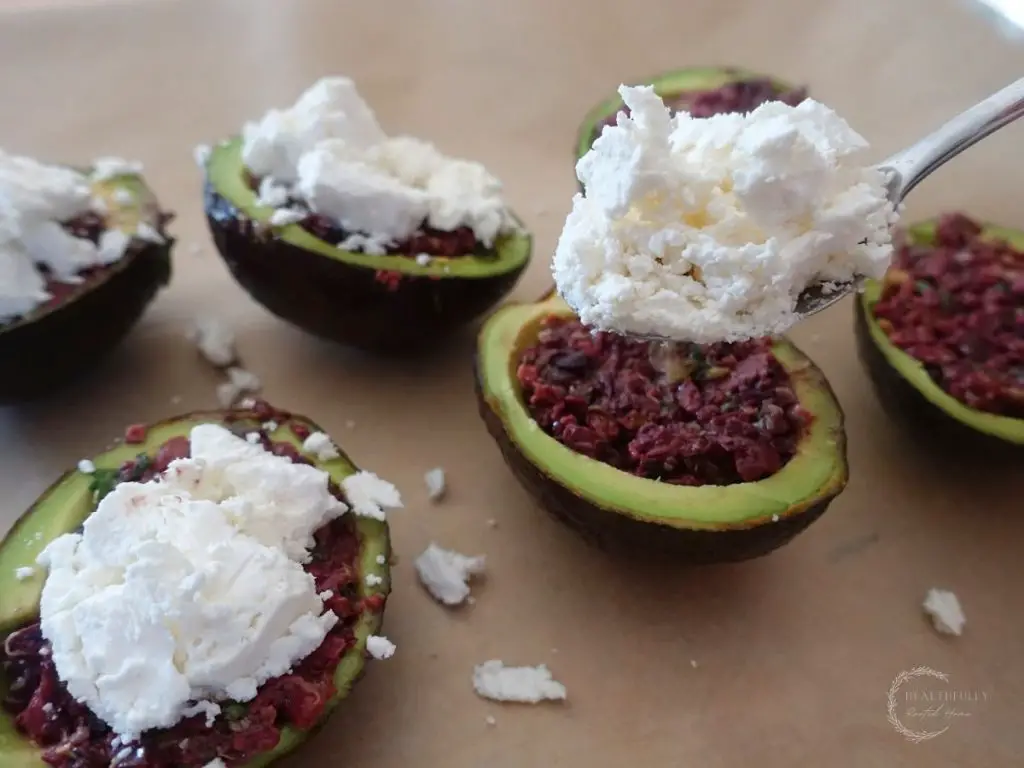 using a silver spoon to top stuffed avocados with goat cheese