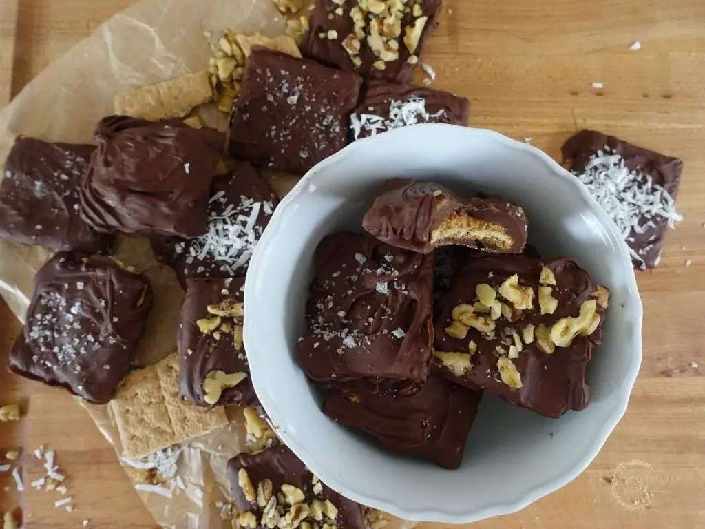 chocolate covered graham crackers in a white bowl stacked on top eachother and on a cutting board spread out