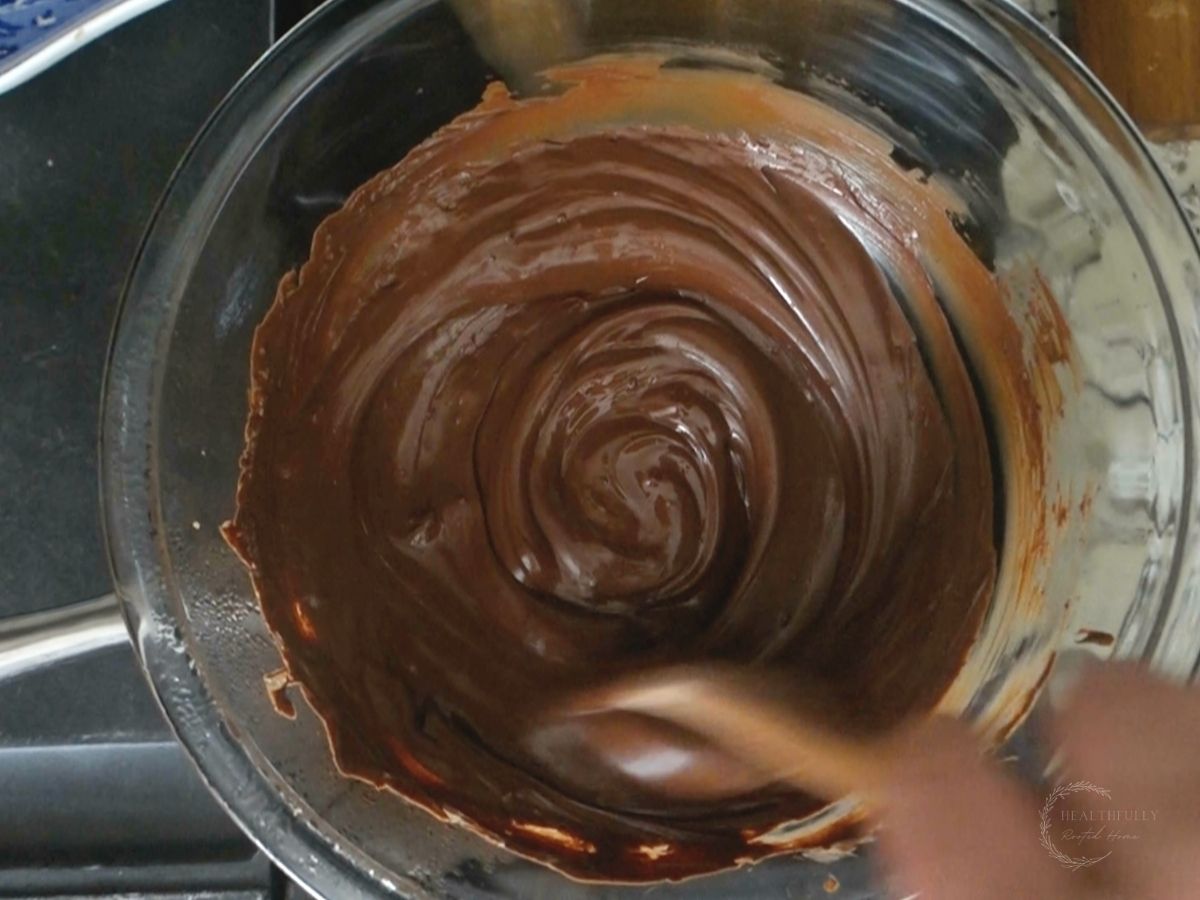 melted chocolate in a double broiler being stirred by a wooden spoon