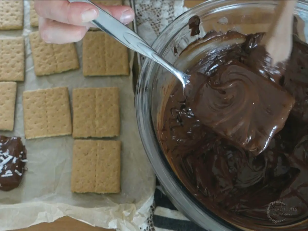 using a fork to pull out a chocolate covered graham cracker and placing on a baking sheet next to graham crackers