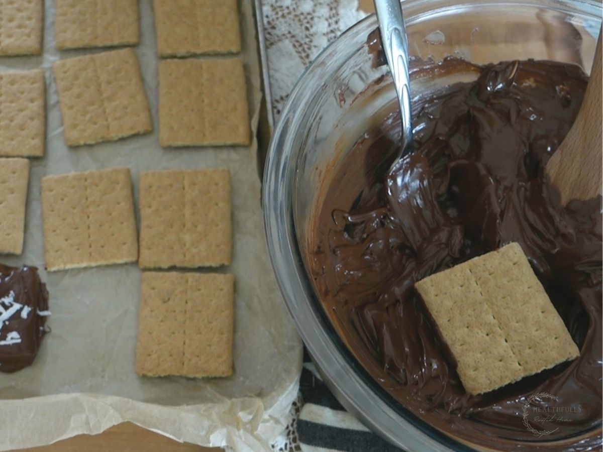graham cracker placed inside a glass bowl of melted chocolate with a fork next to it