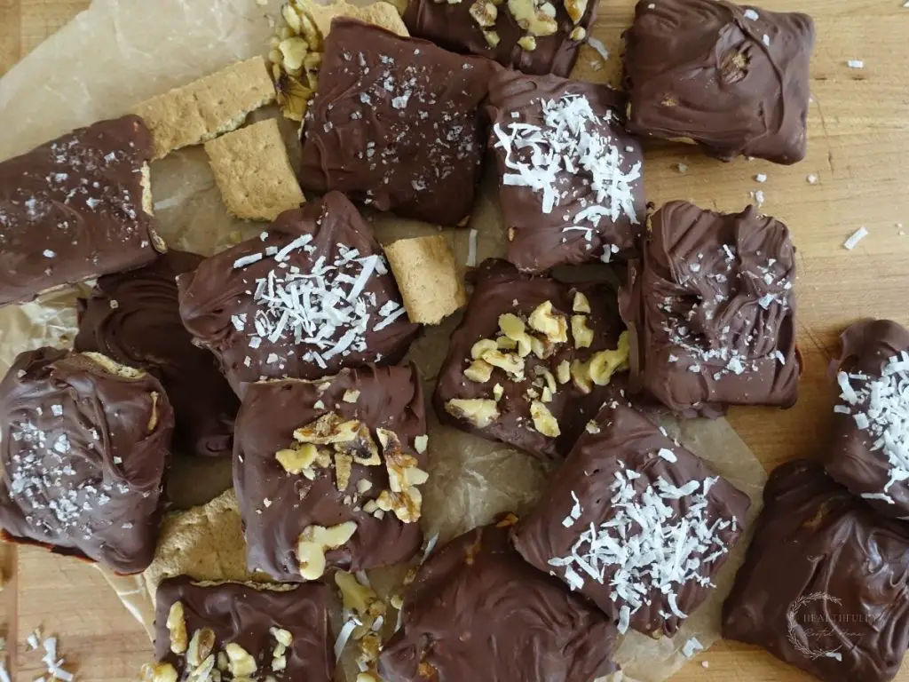 a bunch of chocolate covered graham crackers laid out on a wooden cutting board with a piece of parchment paper underneath