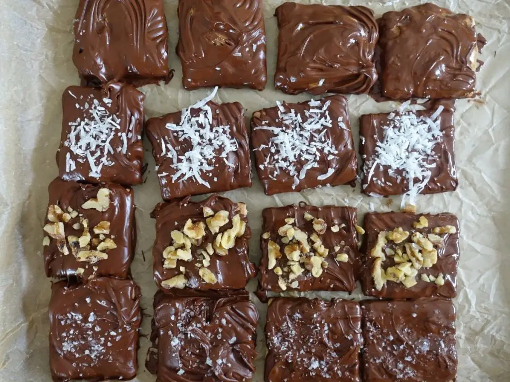 chocolate covered graham crackers on a parchment lined baking sheet with coconut flakes walnuts and sea salt toppings