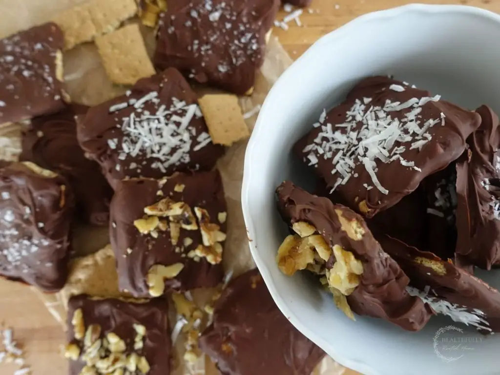 chocolate covered graham crackers spread out all over the wooden cutting board and some inside of a white bowl