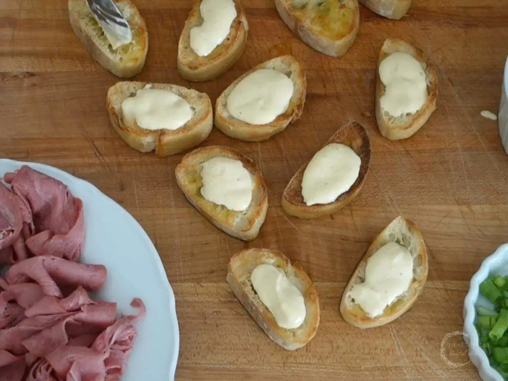 crostini topped with a dollop of horseradish aioli next to a plate of roast beef slices