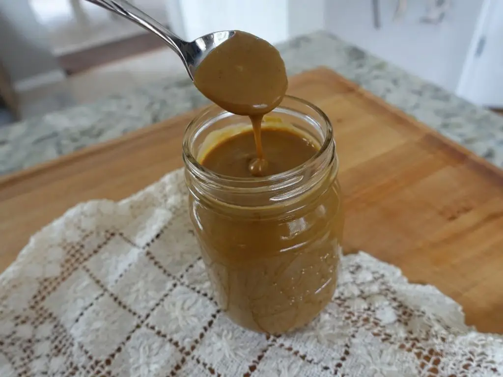 sweetened condensed milk in a mason jar with a doily underneath and a spoon drizzling some back into the jar