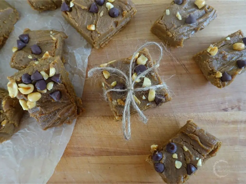no bake peanut butter fudge pieces scattered on top of a wooden cutting board with a couple pieces stacked on top each other tied with a twine bow