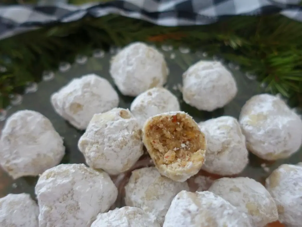 pecan snowball cookies on a glass cake stand with one bitten in half so you can see the inside