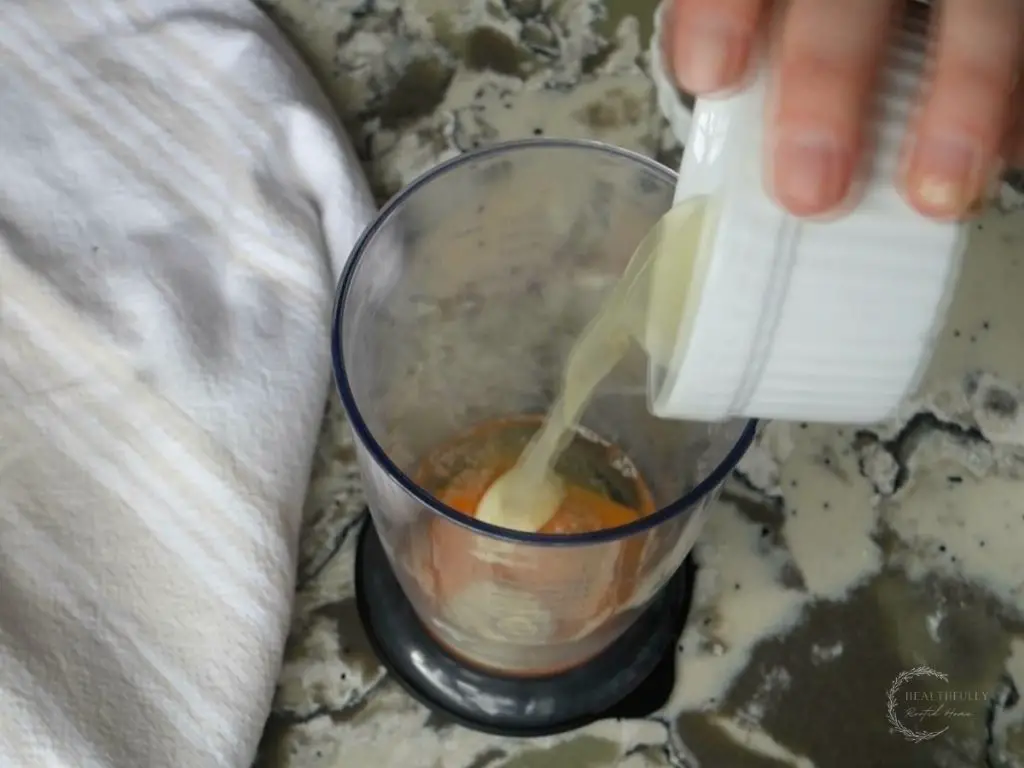 Pouring lemon juice from a white bowl into the cup of an immersion blender