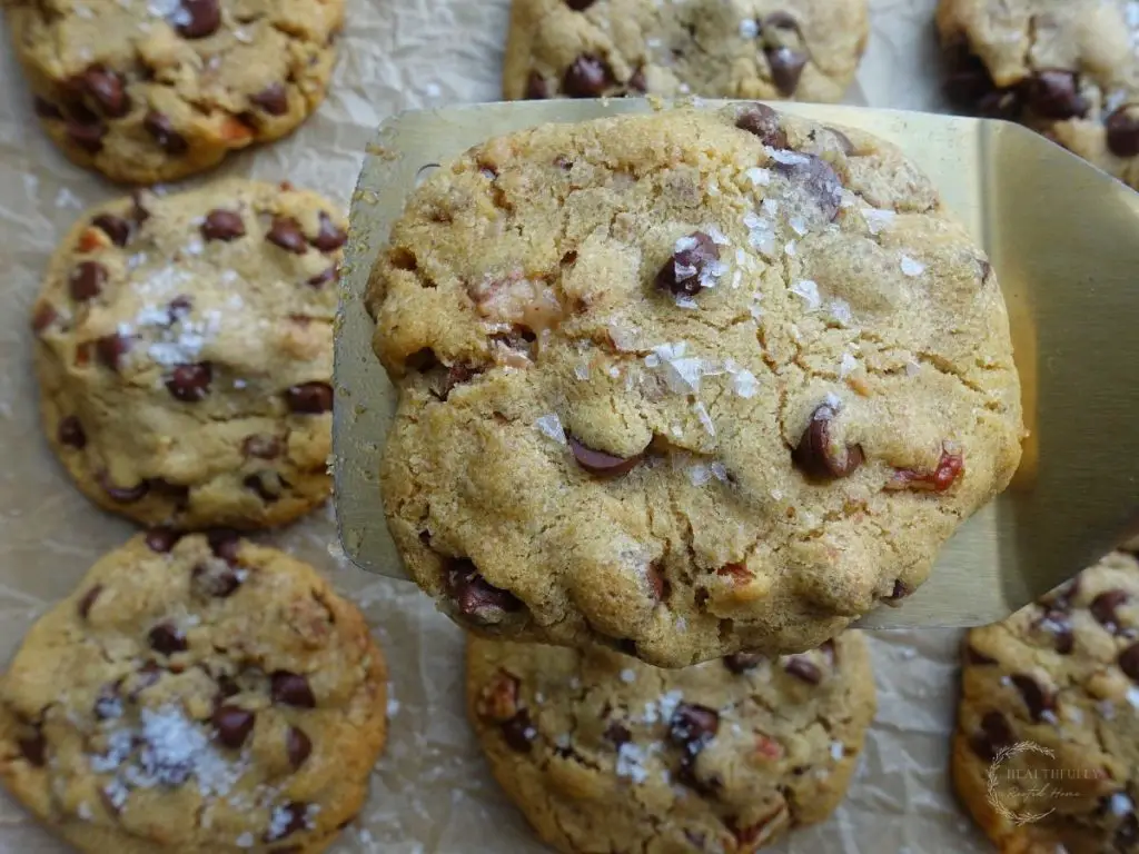 maple chocolate chip cookie held up with a gold spatula with more cookies in the background