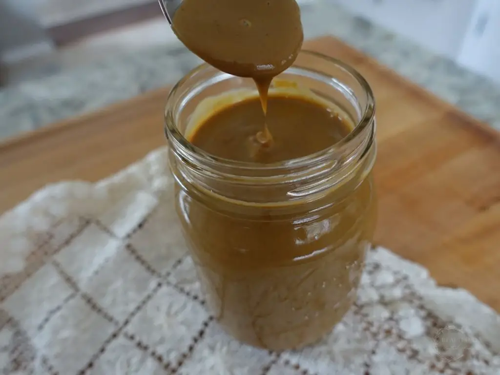 thickened sweetened condensed milk homemade with coconut sugar in a glass mason jar and a spoon drizzling some to see the thickness of it