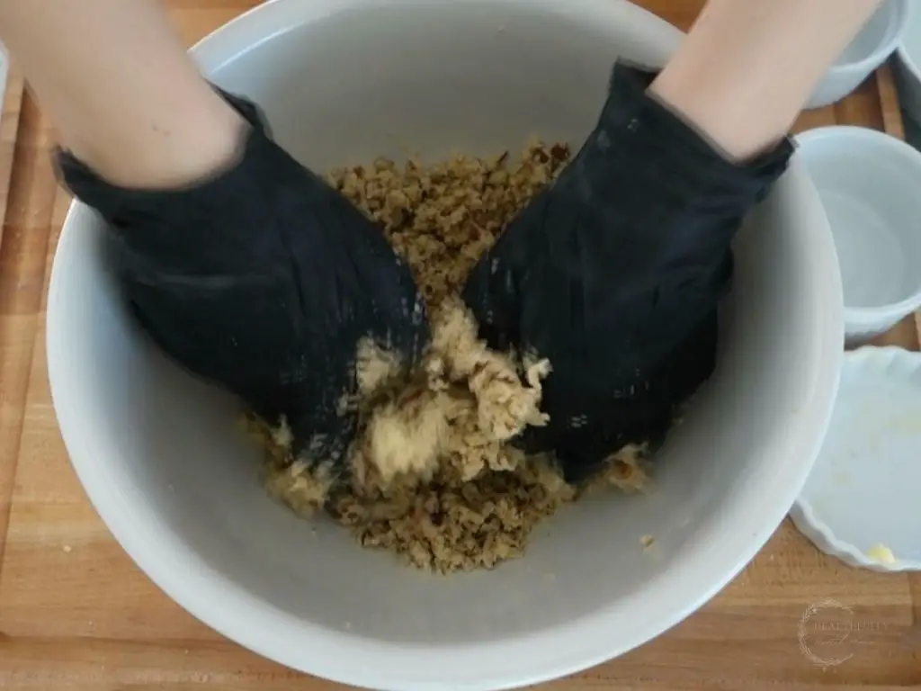 using black gloves to combine ingredients in a large white bowl