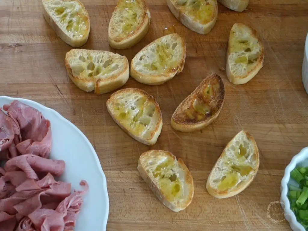 sliced crostini toasted on a wooden cutting board with a plate of roast beef next to them