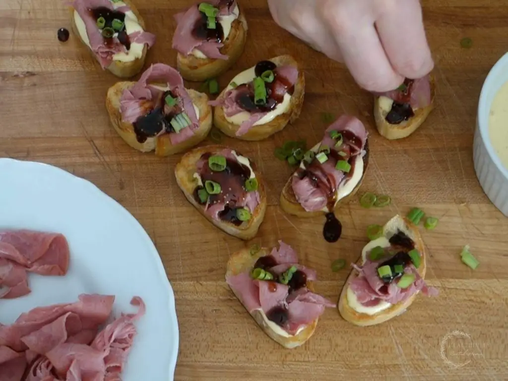 sprinkling green onion on top beef crostini with a plate of roast beef next to them