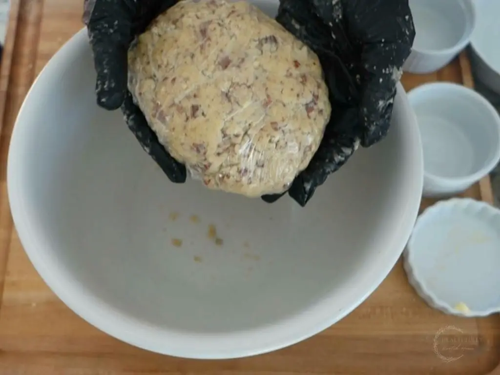 pecan meltaway dough covered in plastic wrap being held with black latex gloves