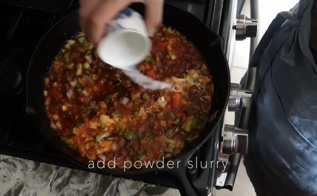 adding powder slurry to the manchurian gravy vegetables in a cast iron skillet to thicken the sauce up
