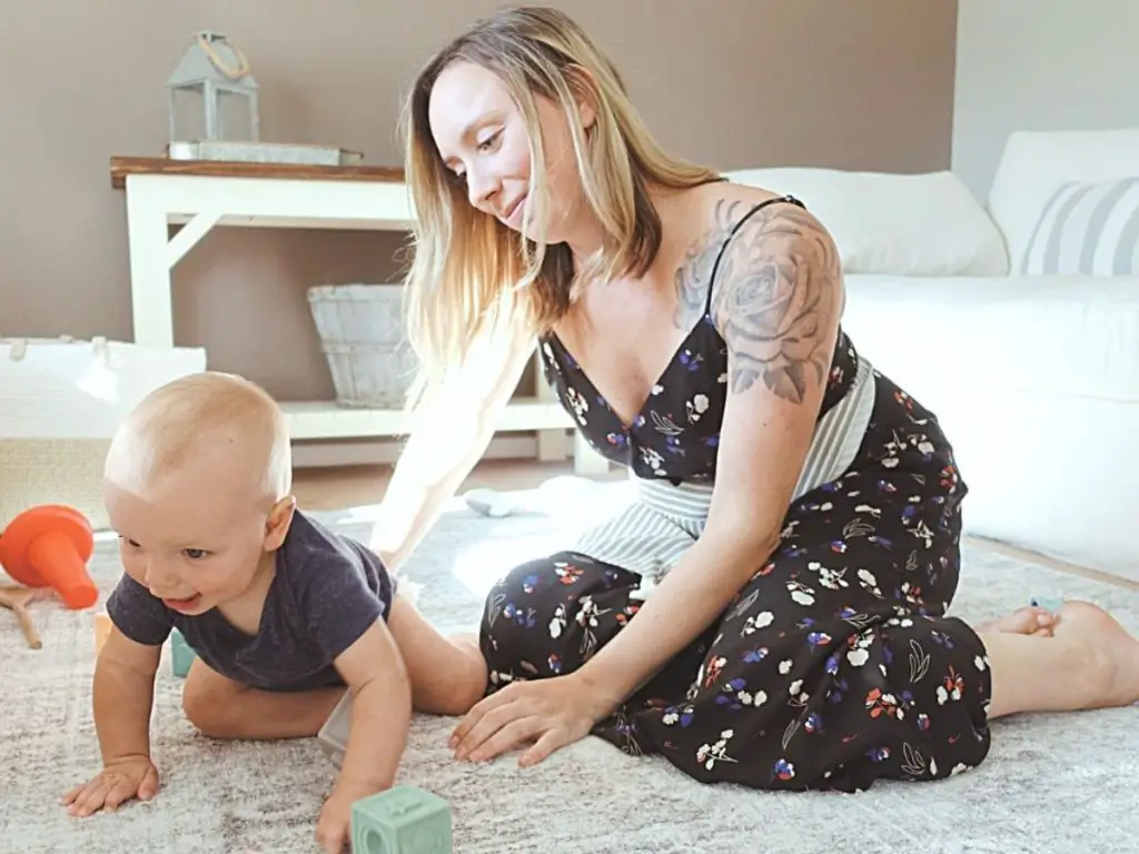 woman with a tattoo wearing a waist apron while playing with her baby on the floor