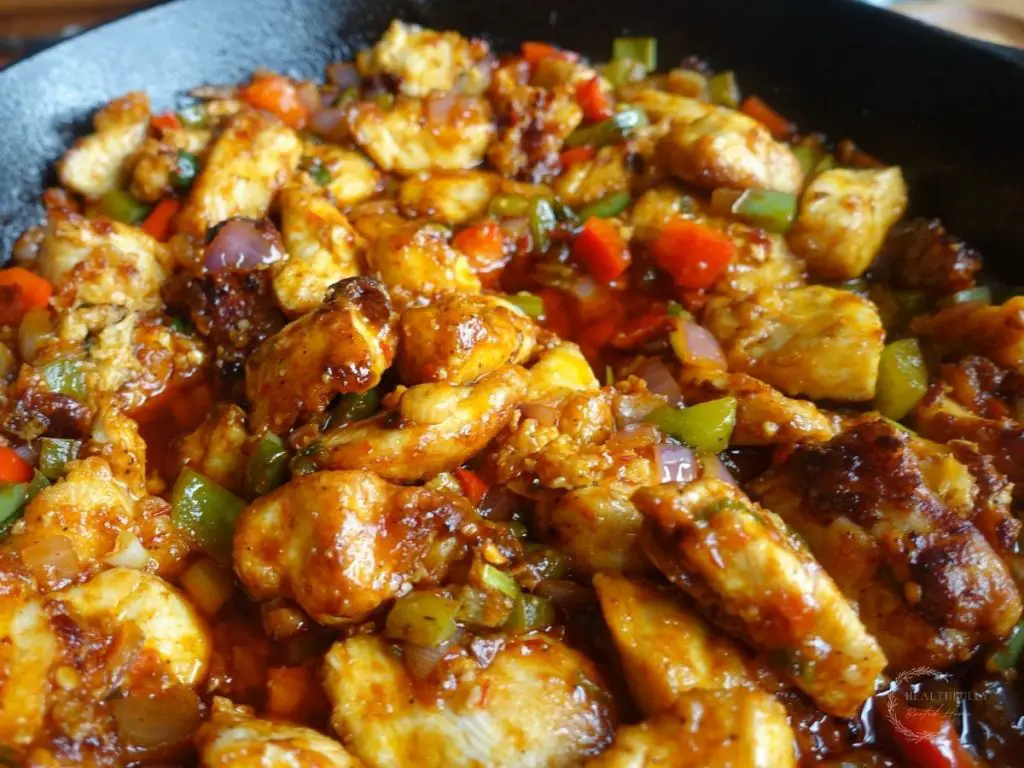 chicken manchurian in a cast iron skillet after being fried and sauteed with the bell peppers, manchurian gravy and red onion