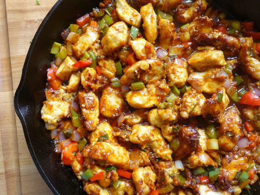 chicken manchurian in a cast iron skillet on top of a wooden cutting board