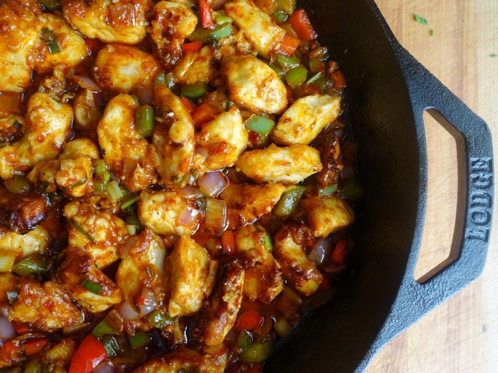 chicken manchurian in a cast iron skillet with red and green bell peppers, red onion, and manchurian gravy