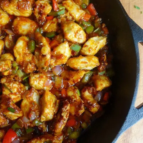 chicken manchurian in a cast iron skillet with red and green bell peppers, red onion, and manchurian gravy