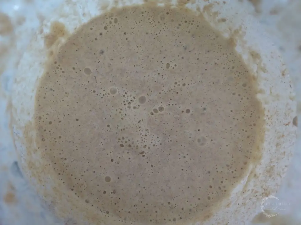 sourdough starter in a glass container with a lot of bubbles on top