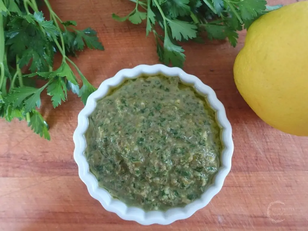 salsa gremolata in a white dish on a wooden cutting board with a lemon and parsley next to it