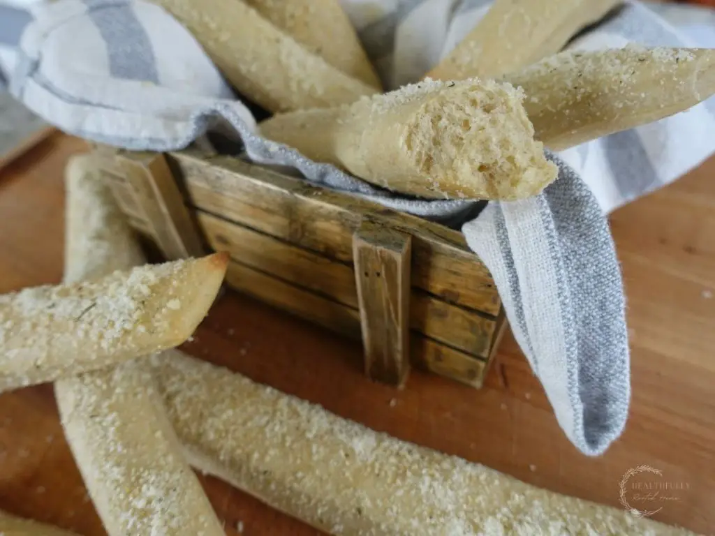 sourdough breadsticks with garlic parmesan topping in a wooden basket with a blue and white tea towel